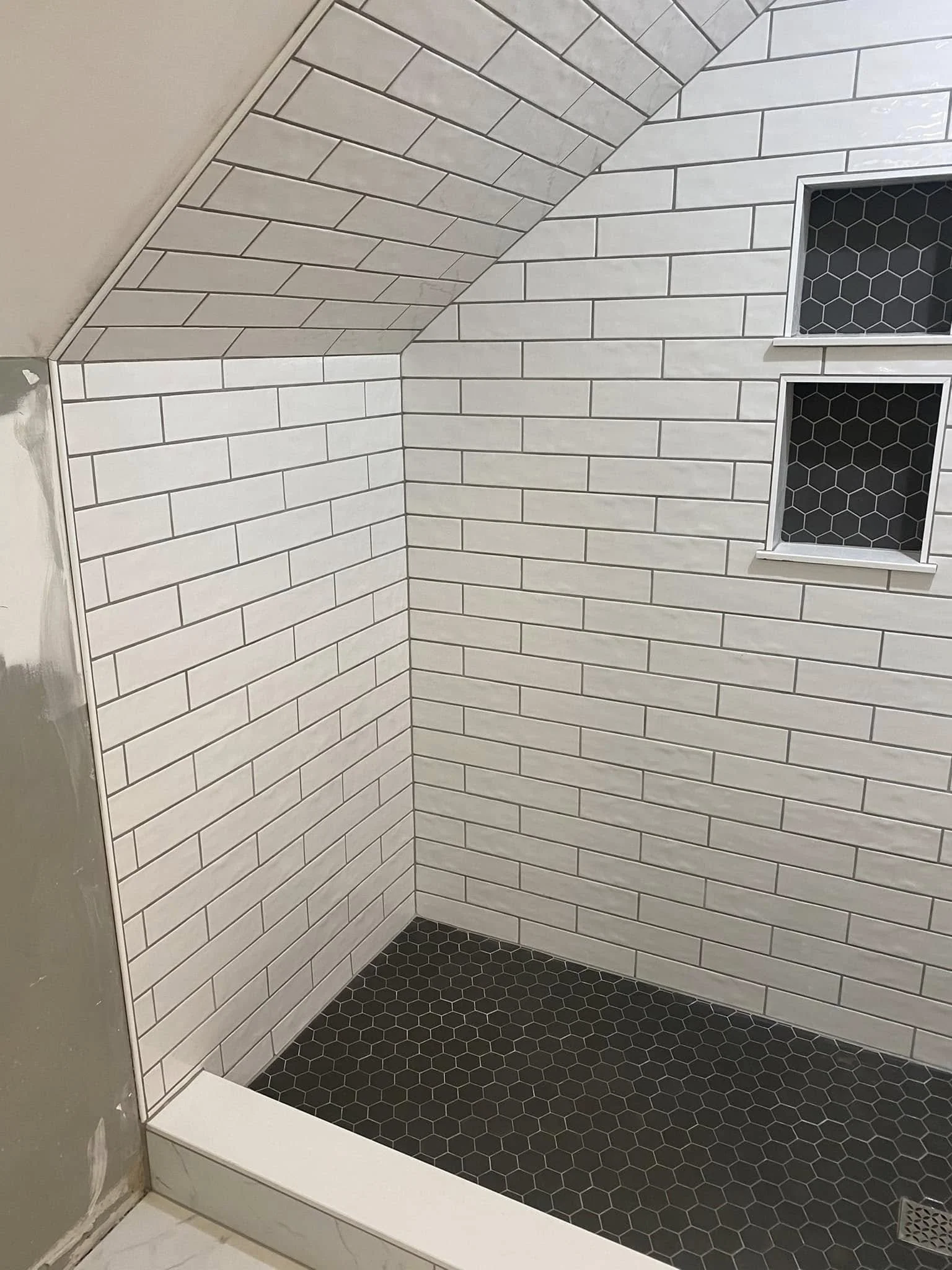 A shower area with white subway tiles on the walls and black hexagonal tiles on the floor and in the recessed shelf.