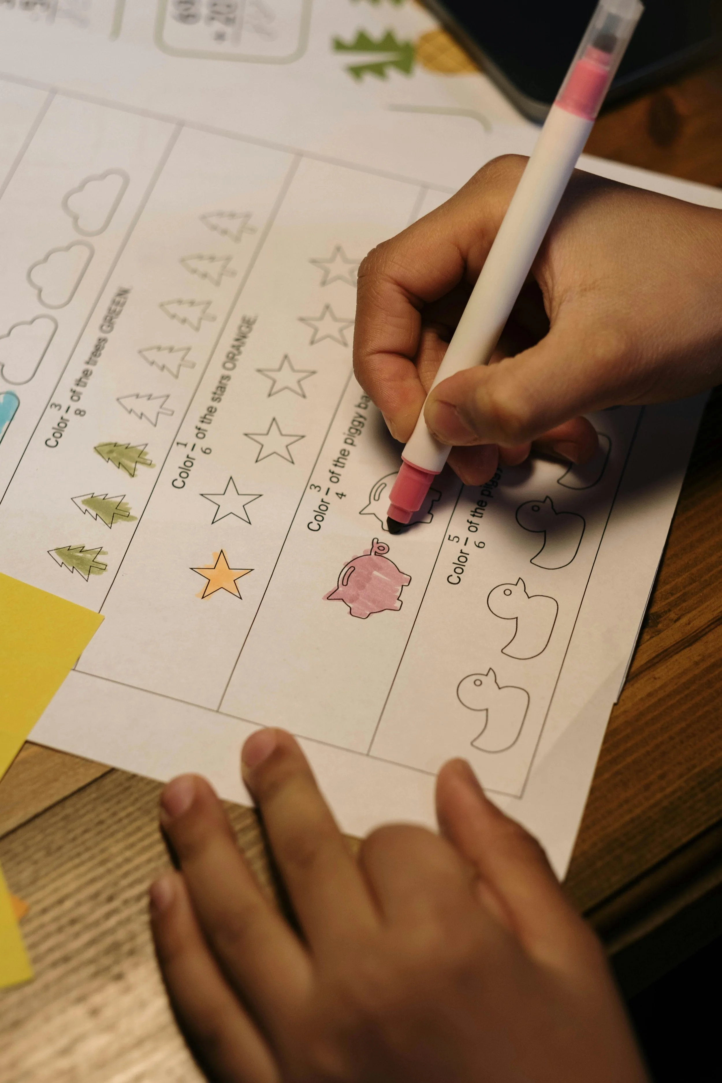 Children are coloring holiday-themed worksheets with outlines of Christmas trees, stars, and Christmas pigs, using colored markers.
