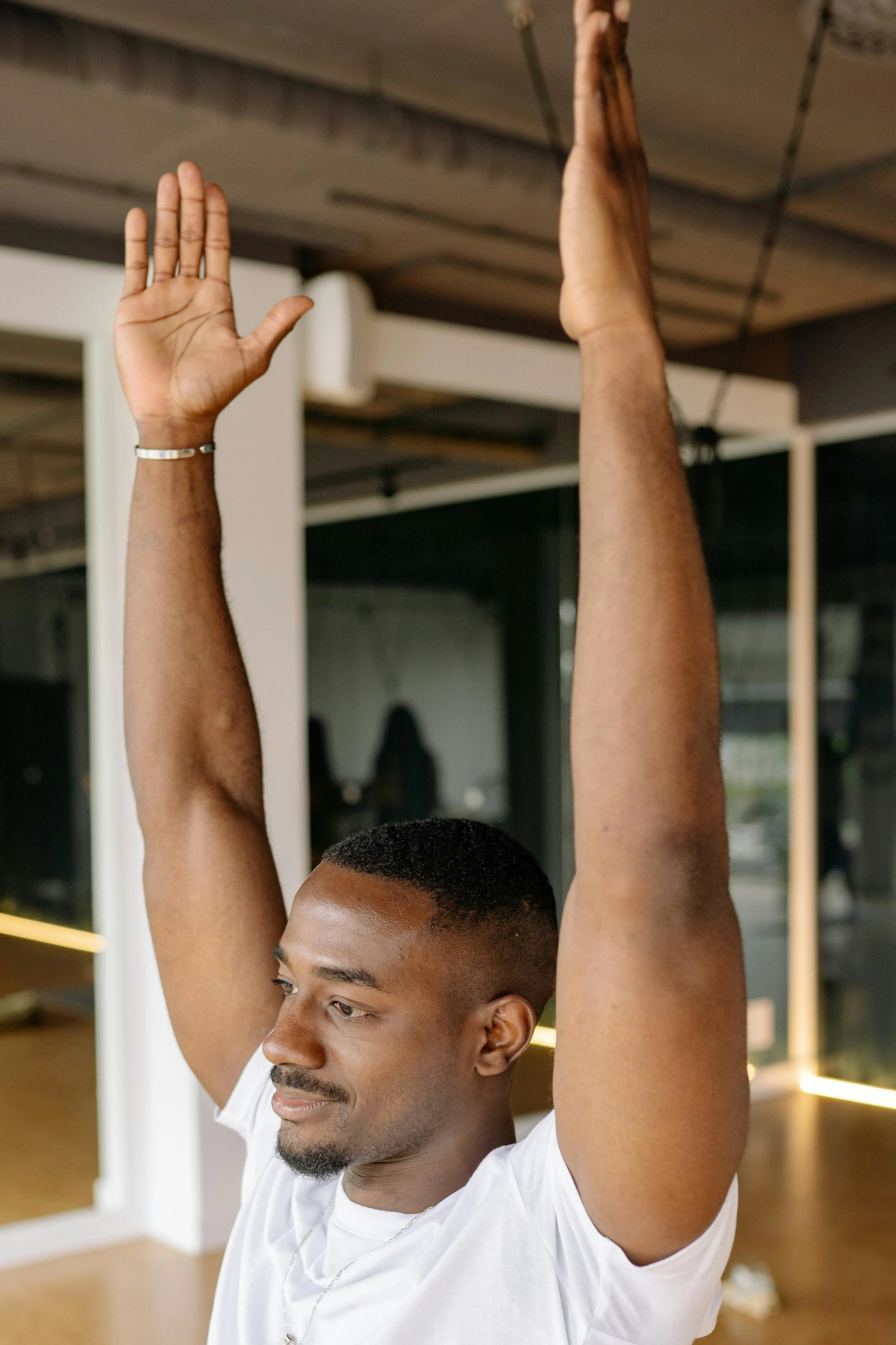 Un homme noir faisant du yoga, assis avec les yeux fermés, bras levés, dans une pièce moderne
