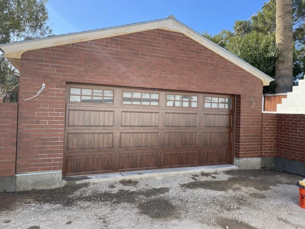 Photo of a new garage with a wood-paneled garage door and red brick walls, against a background of blue sky and trees.