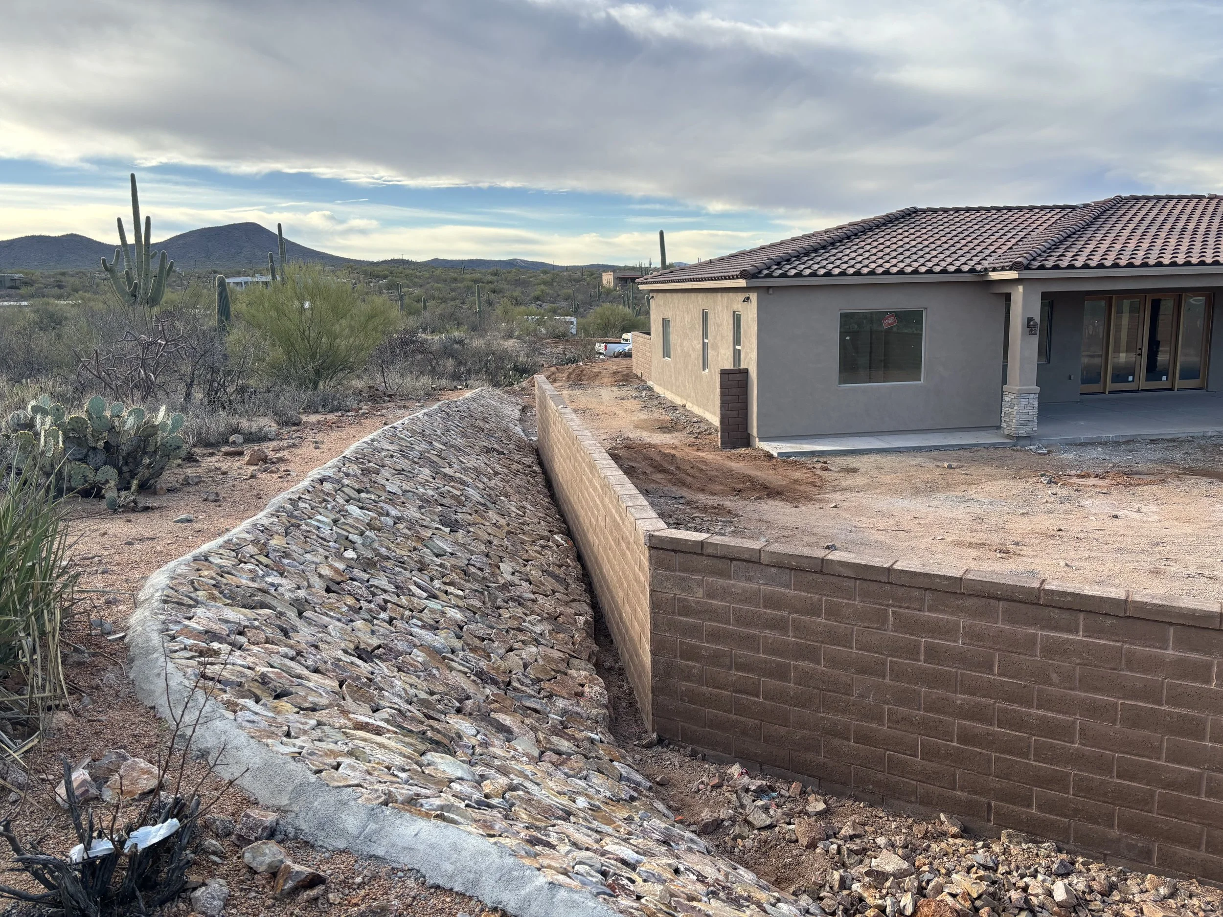 New house under construction in desert landscape with cacti, hills in background, and cloudy sky.