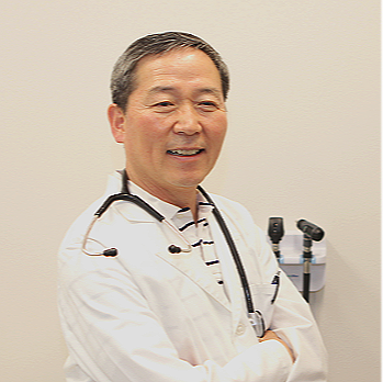 Smiling doctor with stethoscope standing with arms crossed in a medical office.