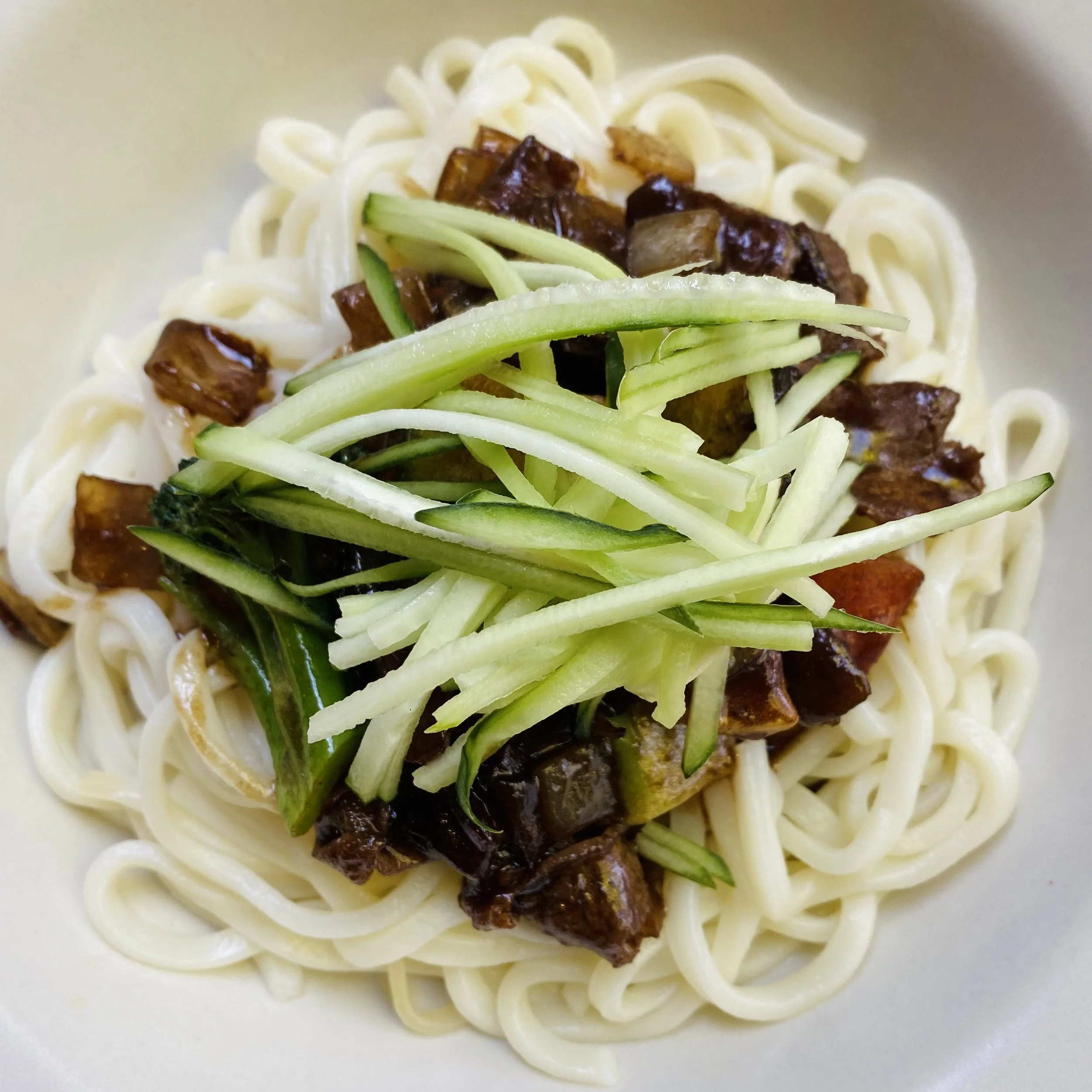 Close-up of a bowl of cooked spaghetti noodles topped with chopped zucchini and sautéed beef chunks.