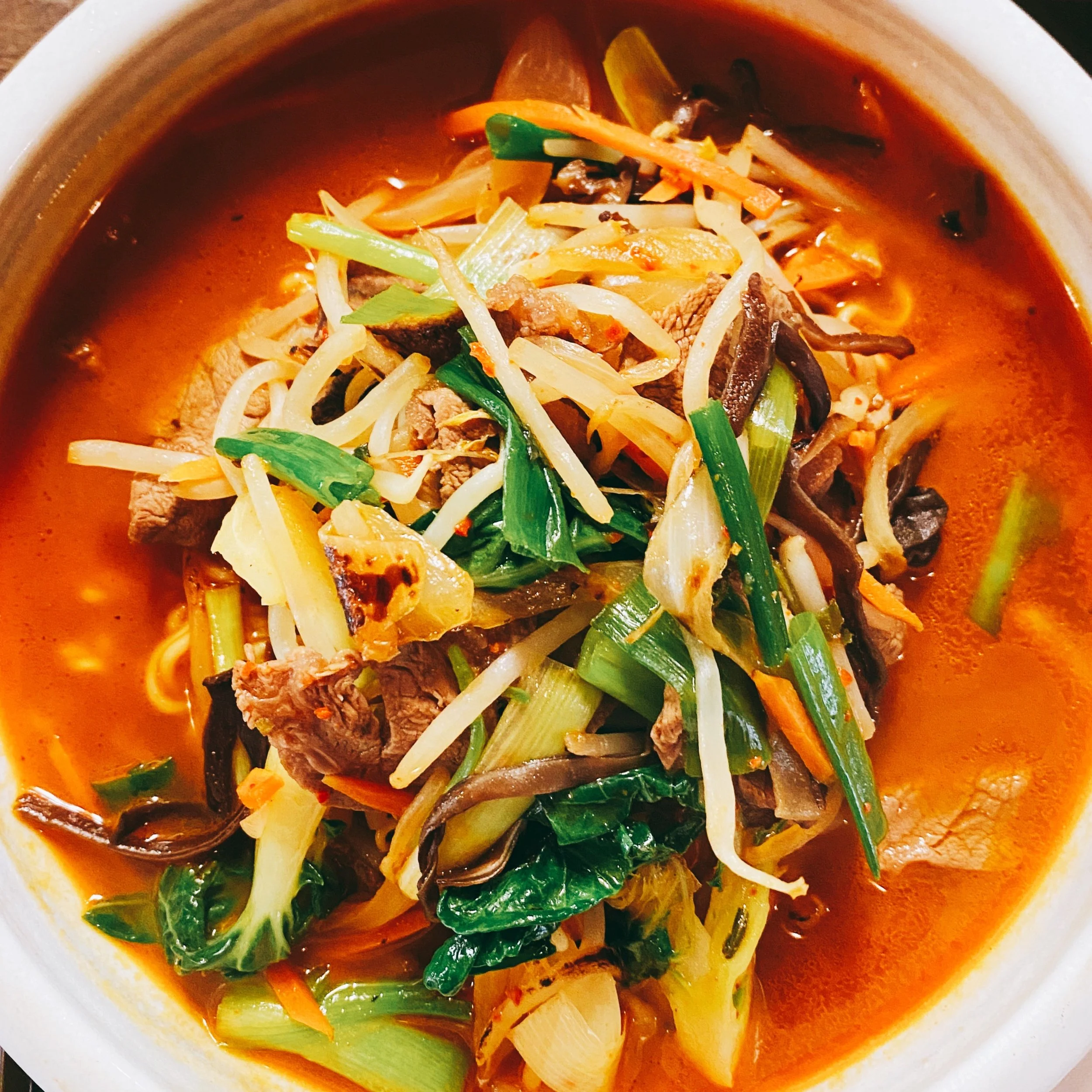 A bowl of hot soup with various vegetables, sliced meat, and a spicy red broth.
