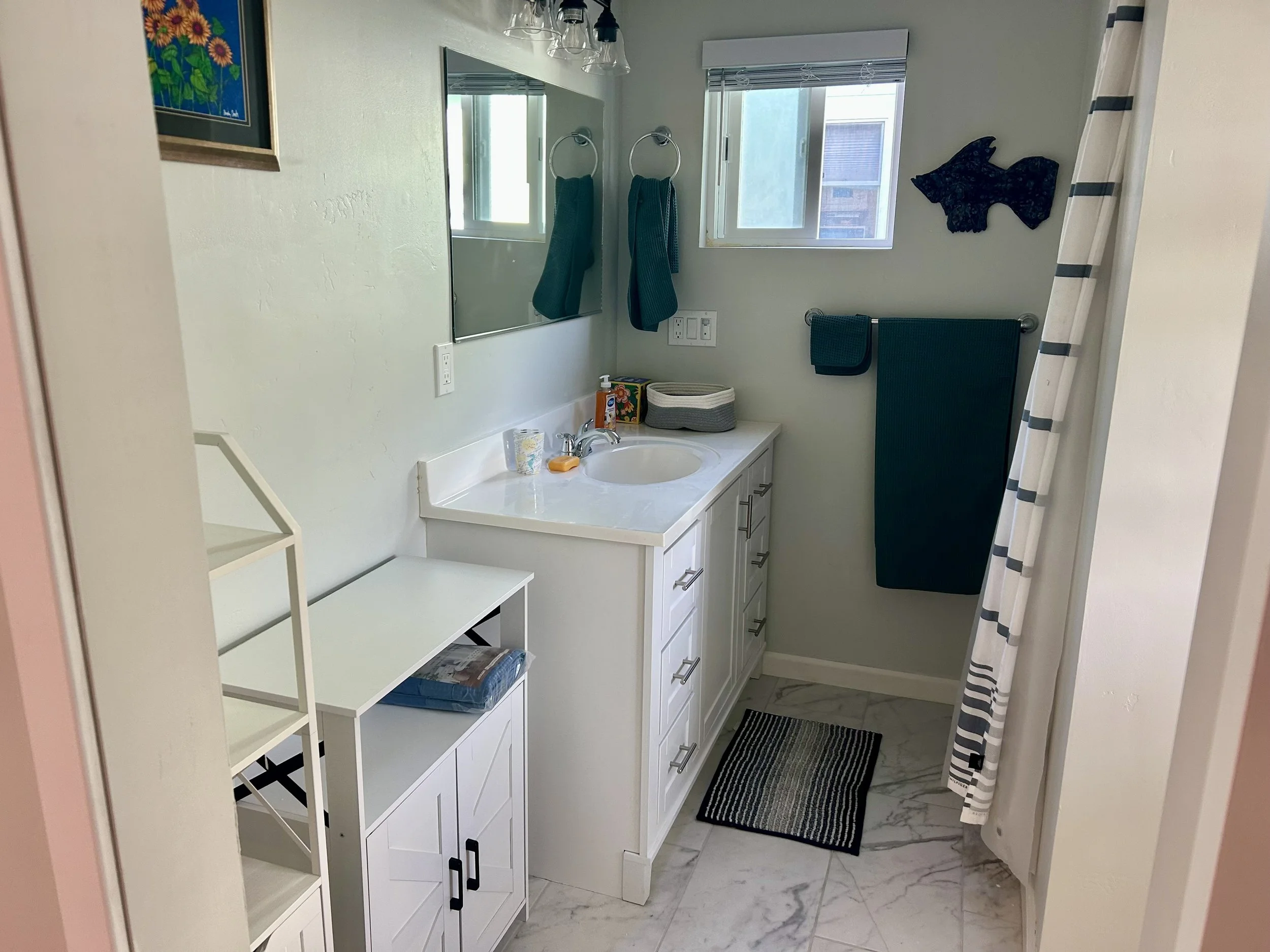 A bathroom with a white vanity cabinet, a mirror, and bathroom essentials.