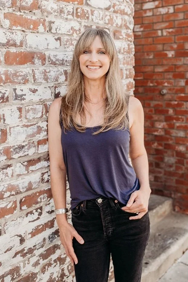 Melissa founder of KAIA Consulting, standing against a faded brick wall