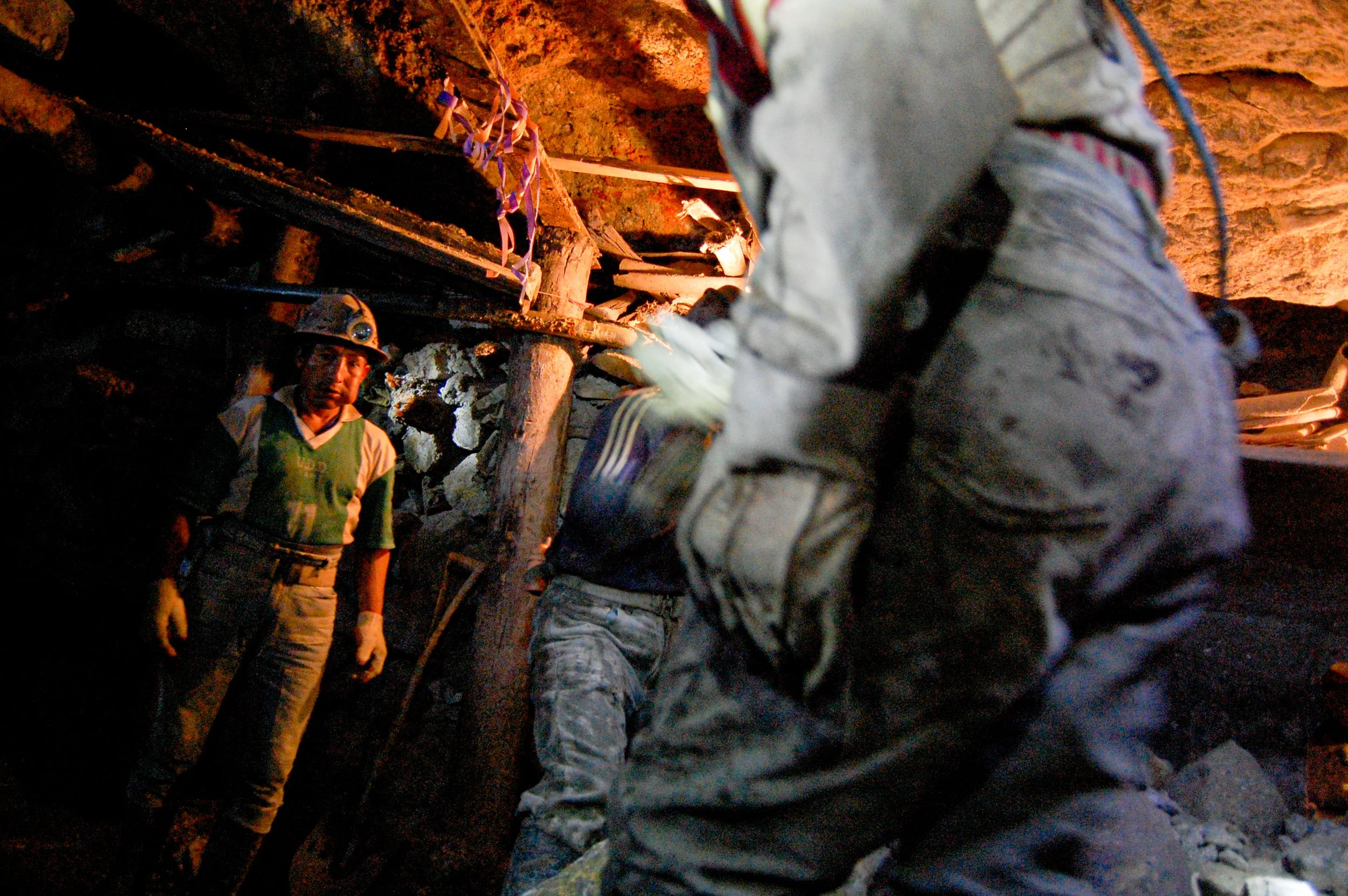 Mensen dragen helmen en werkoutfit terwijl ze in een ondergrondse mijn werken, omgeven door rotsen en metalen constructies.