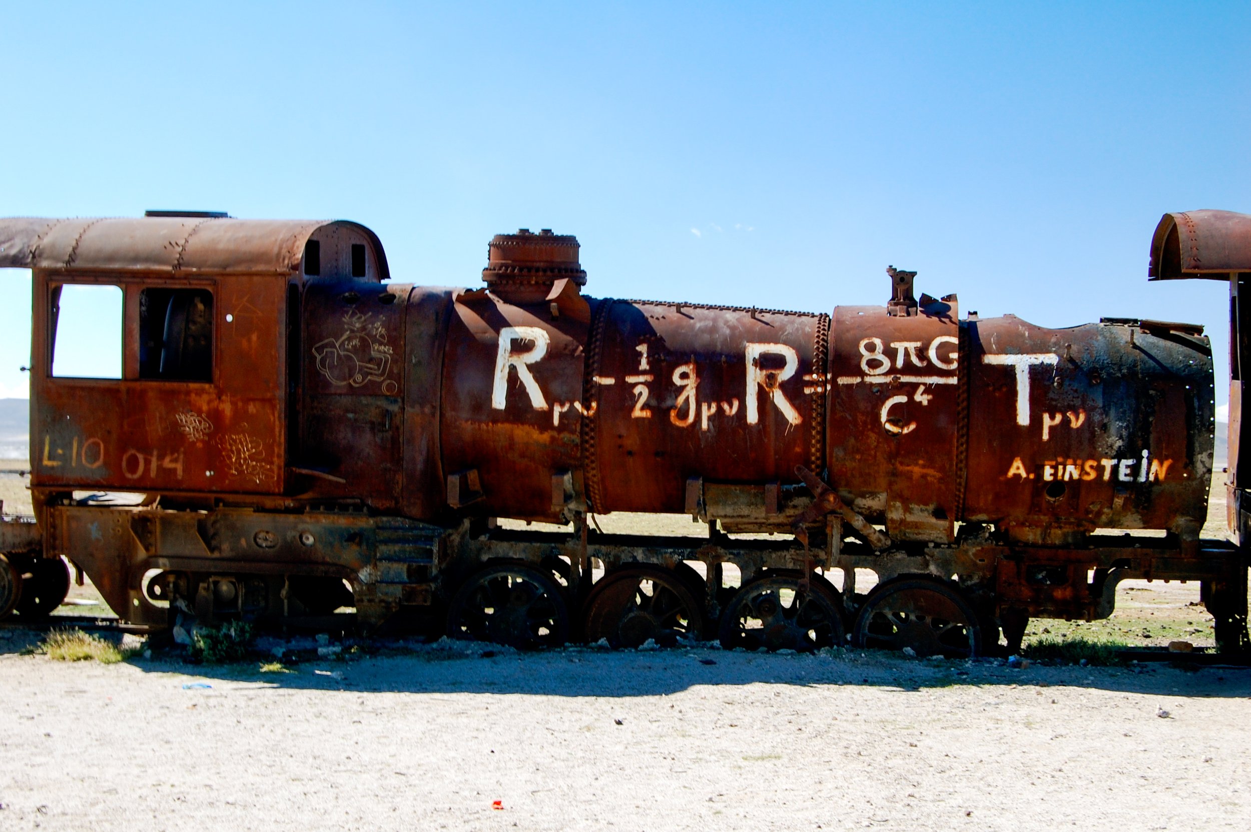 Een oud, roestig stoomlocomotief rustend op een stuk land onder een heldere blauwe hemel.