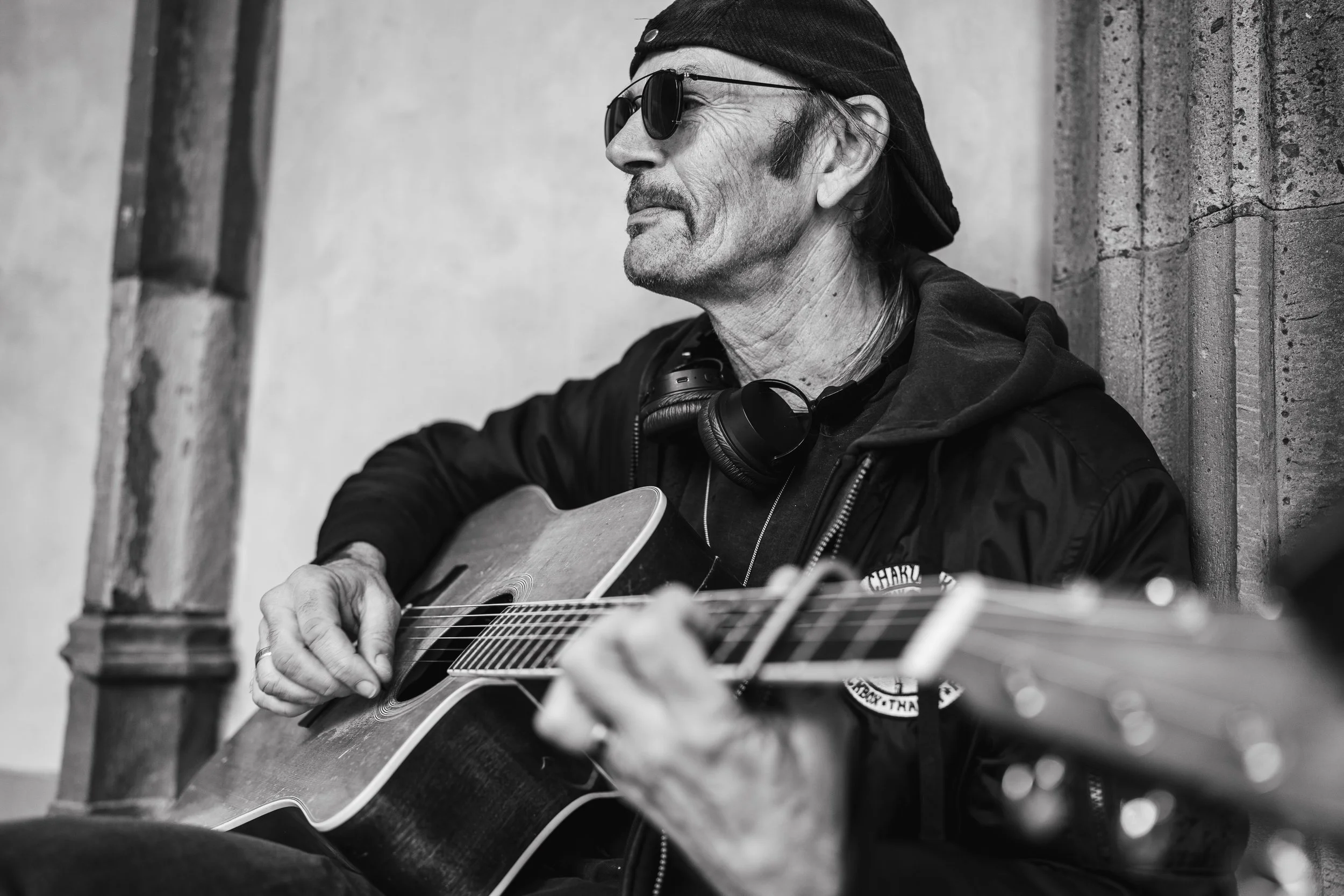 Een man met een hoed en sunglasses speelt gitaar tegen een muur.