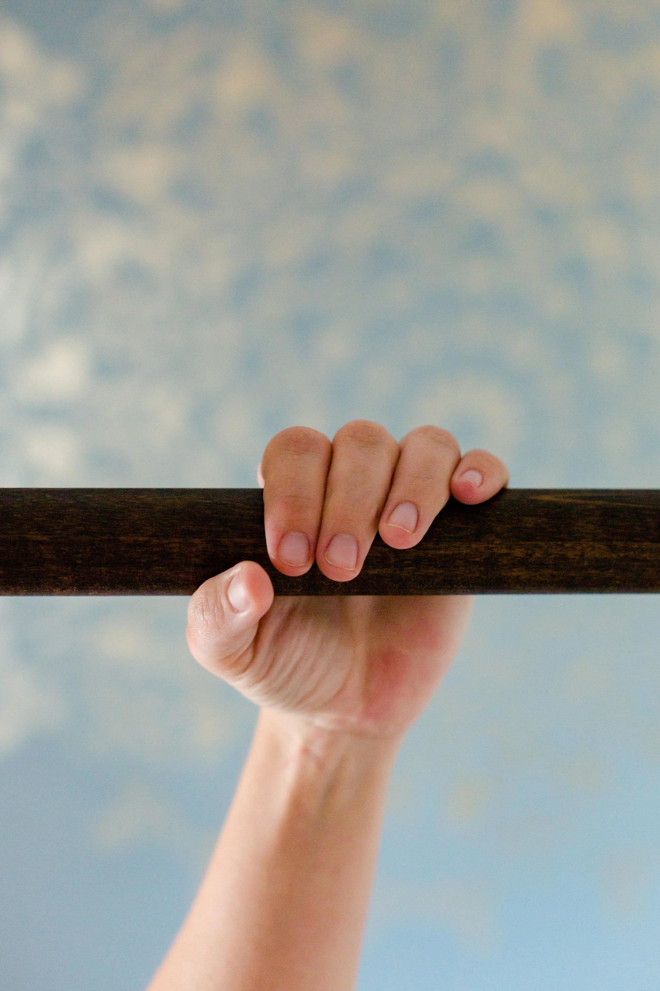 A person's hand holding a ashiatsu bar with a blue and gold wall in the background.