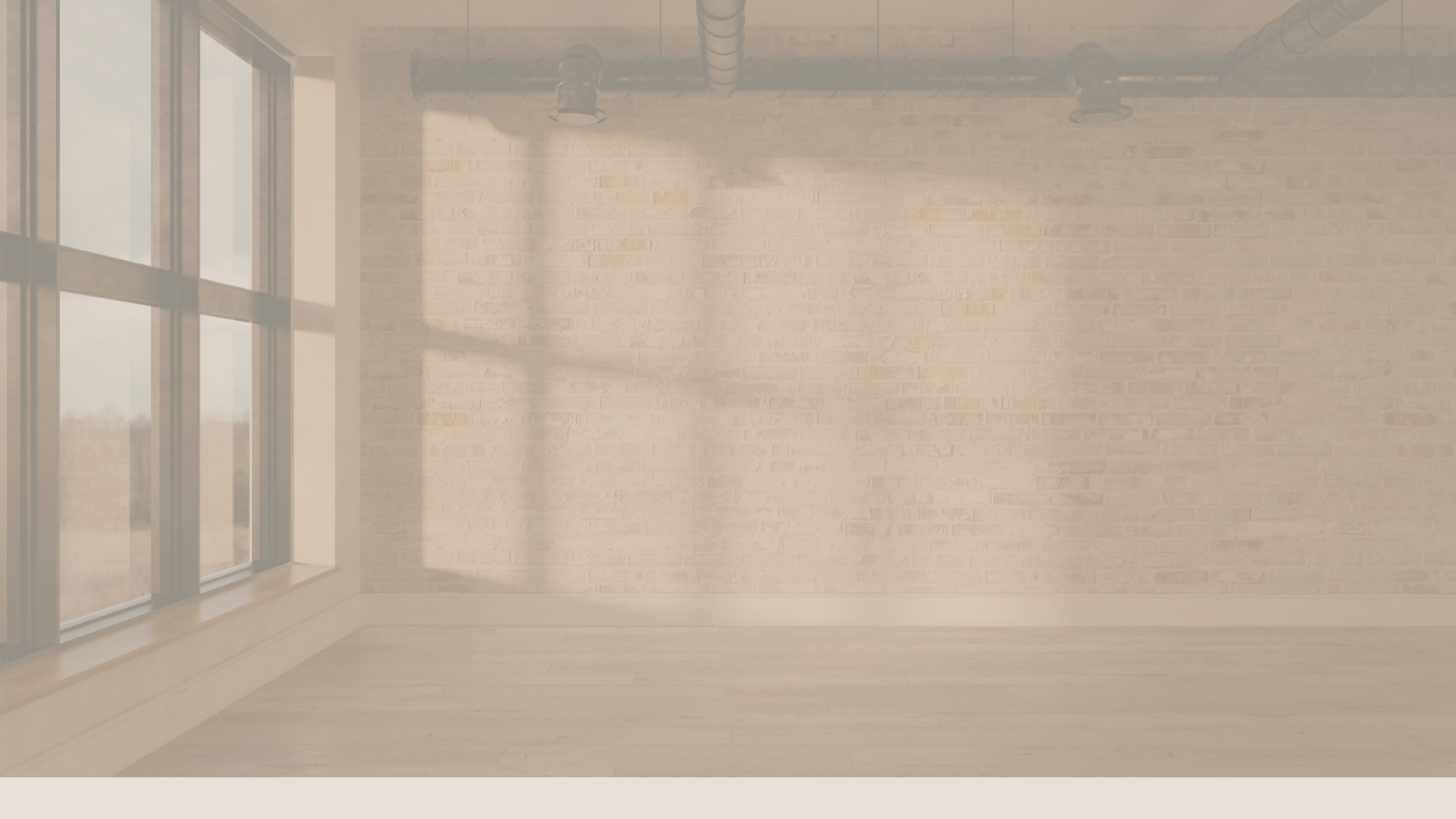 Empty room with large window on the left, exposed brick wall, wooden flooring, and visible ceiling pipes with sunlight casting shadows on the wall.