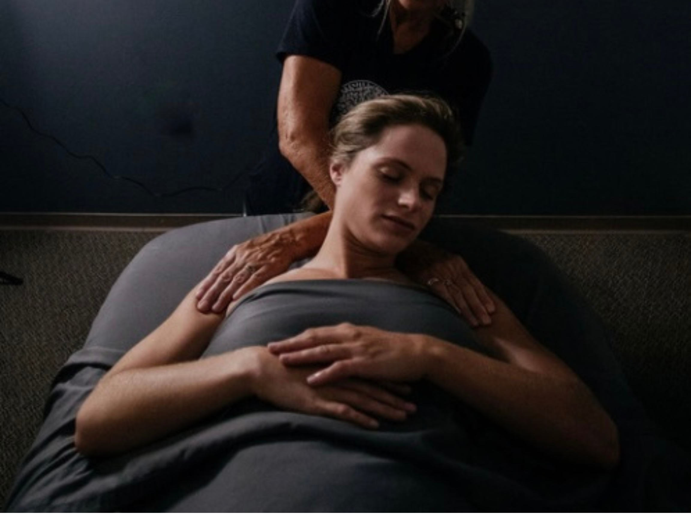 A woman lying face up on a massage table receiving a neck massage from a massage therapist.