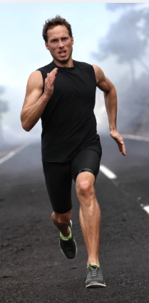 A man in black athletic clothing running on an open road under cloudy skies.