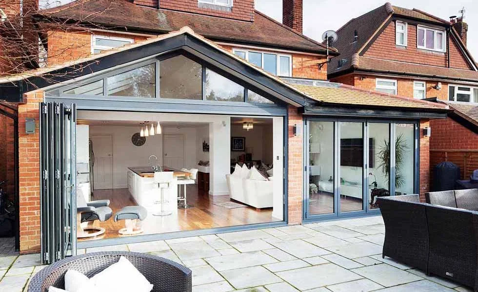 Open sliding glass doors lead from a patio to a modern kitchen and living area in a brick house.