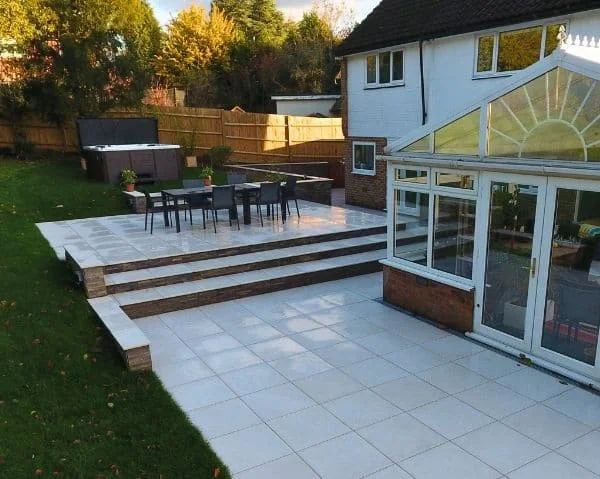 Backyard patio with steps, outdoor dining table, and a greenhouse adjacent to a house.