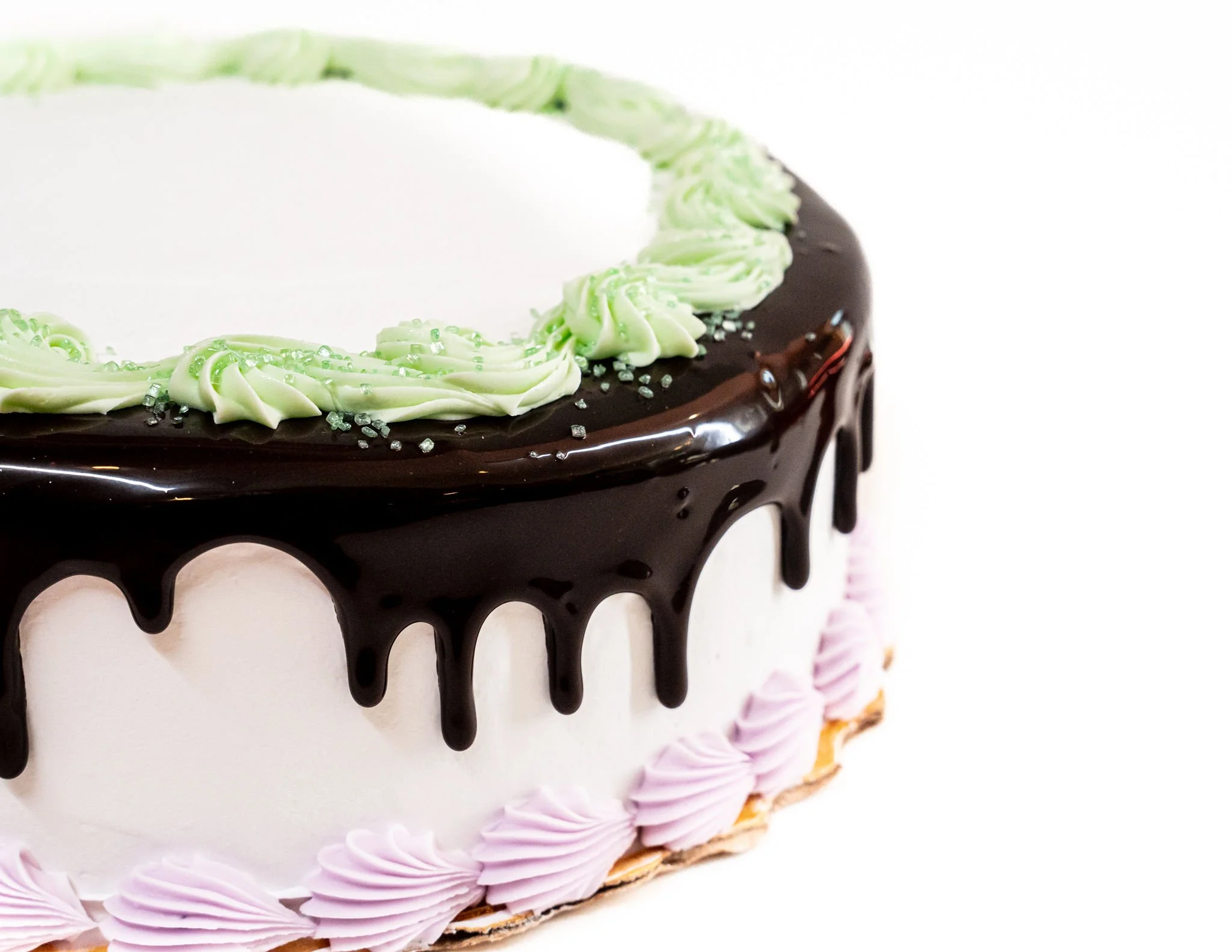 A decorated birthday cake with dark chocolate ganache dripping down the sides, green and pink icing decorations, and sugar pearls, set against a plain white background.
