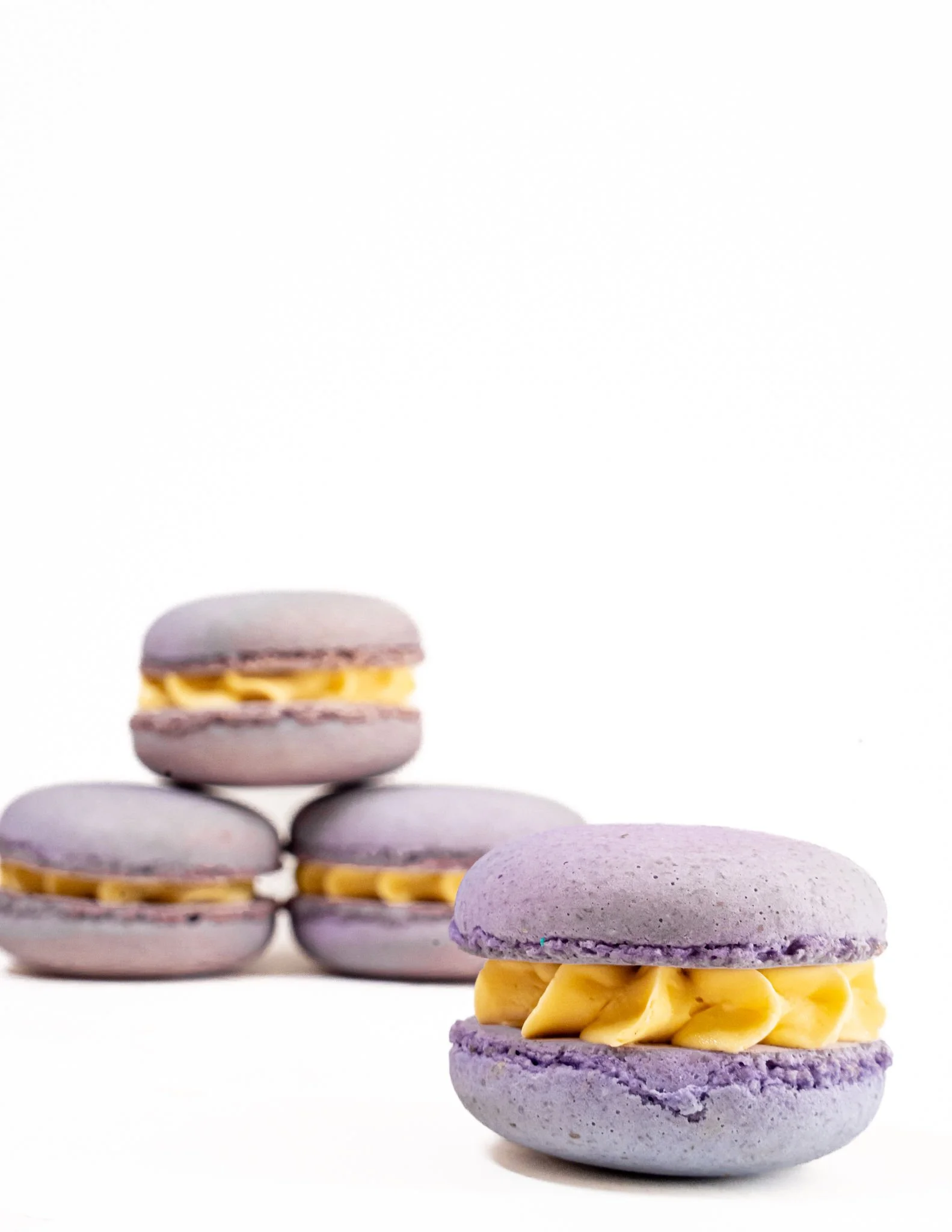 Close-up of purple macarons with yellow filling, stacked on a white background.