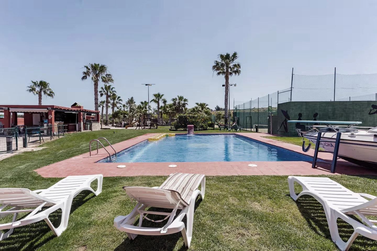 spain motocross holiday holidays with ride europe. Swimming pool with lounge chairs and palm trees in a sunny outdoor setting