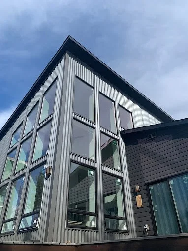 Modern building with large windows and metal siding, seen from below against a blue sky.