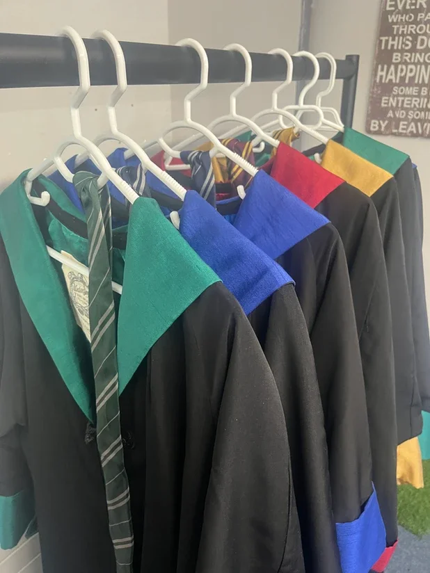 A row of Hogwarts gowns hanging on white hangers, each with a different colored collar and matching accents.