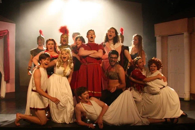A theatrical stage with a group of actors in roman costumes posing and performing.