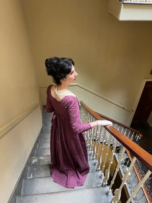 A woman dressed in historical clothing descending a spiral Georgian staircase, with her dark hair styled up.