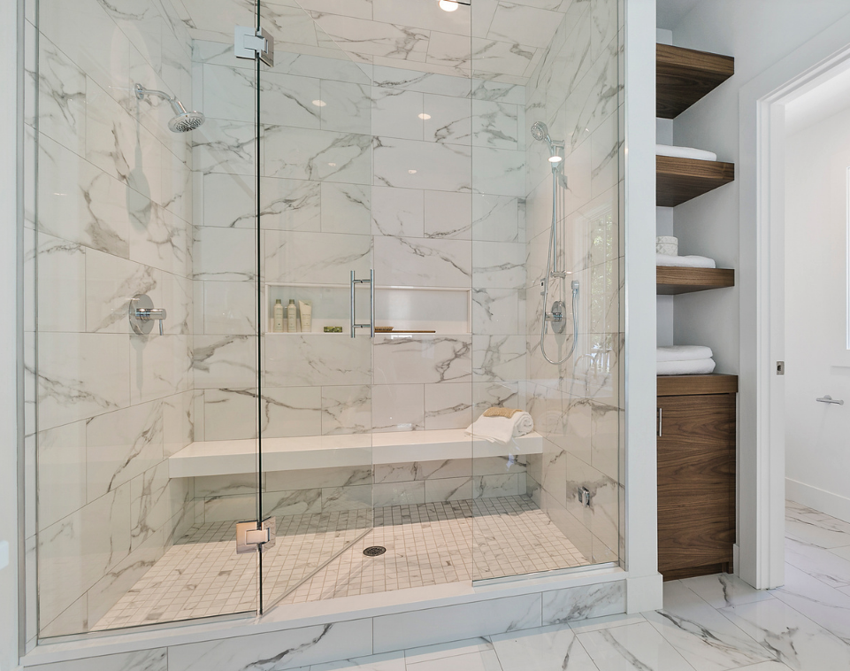 A luxury primary bathroom featuring a spacious walk-in shower with white marble walls and a seamless glass enclosure, built-in shower bench, floating wood shelves, and matching marble floor tiles.