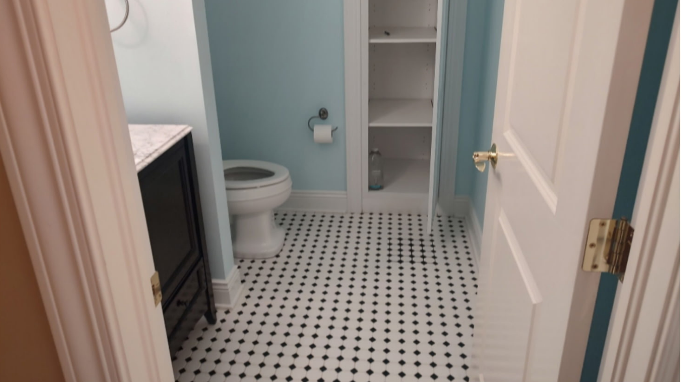 Small bathroom with black and white checkered tile floor, a toilet, open white shelving unit with a water bottle, and a dark vanity with a marble countertop.