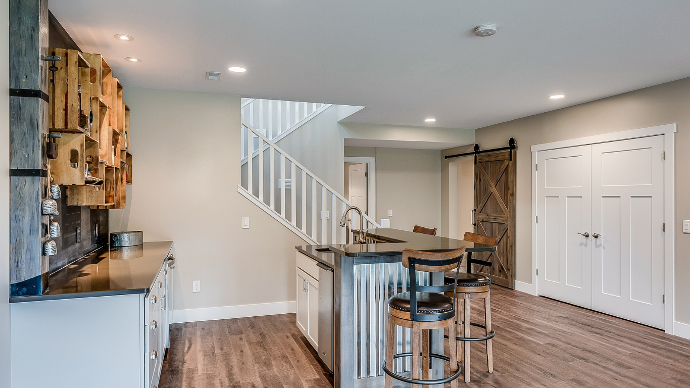 Rustic basement bar with a corrugated metal island counter, wooden barstools, a wooden crate wall display, and a sliding barn door.