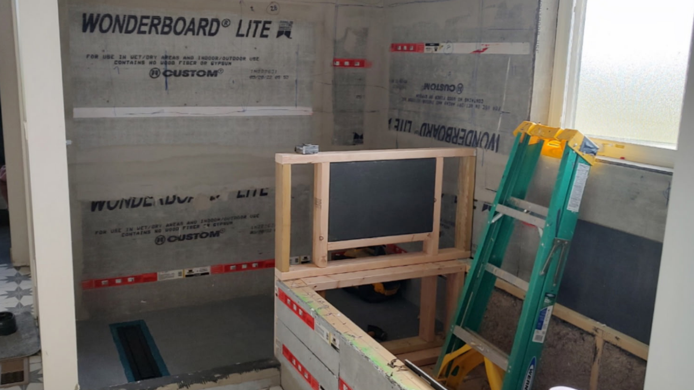 Walk-in shower build under construction featuring WonderBoard Lite cement backer board installation. A custom pony wall frame sits ready for tile prep inside the unfinished residential bathroom build site.