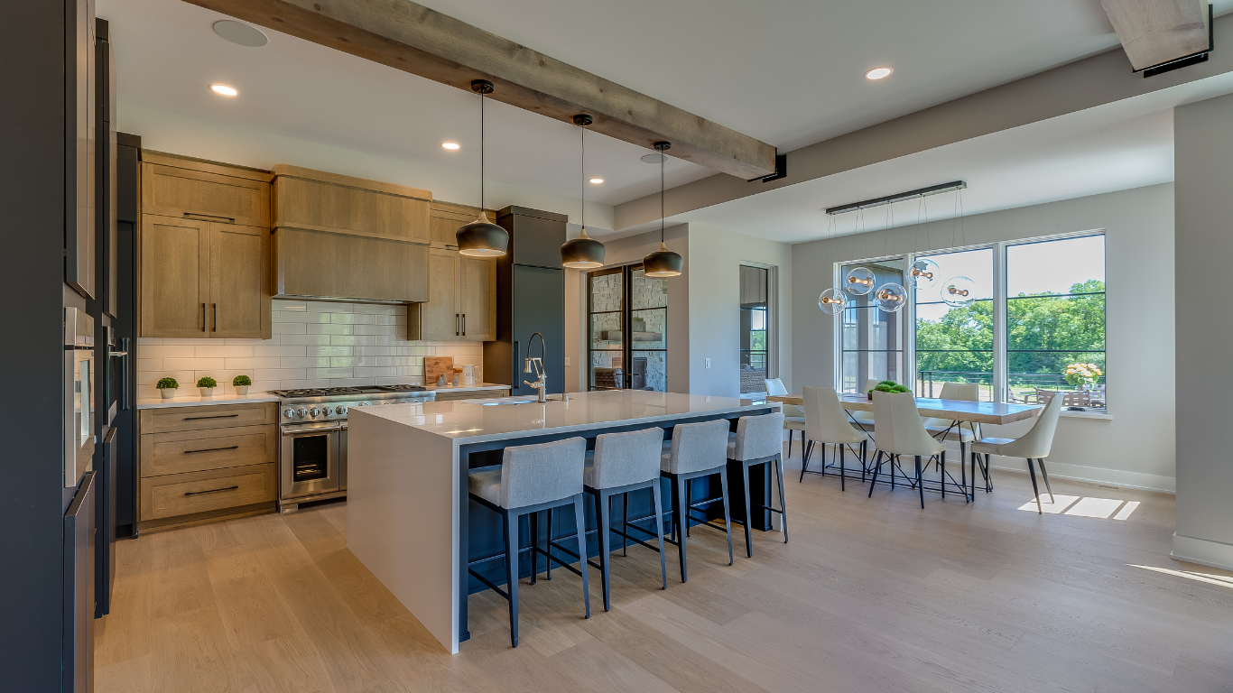 Modern kitchen remodel featuring light oak cabinets, a white quartz waterfall island with bar stools, dark pendant lights, and a rustic wood ceiling beam.