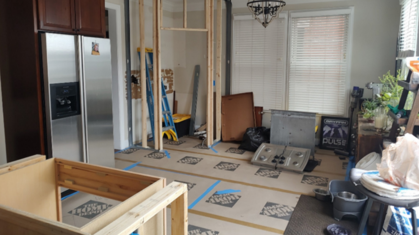 Living room under renovation with construction materials, tools, and partially completed framing.