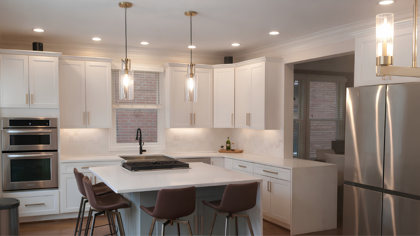 Finished white kitchen cabinet refacing project featuring a large quartz island with seating, stainless steel appliances, and gold pendant lighting.