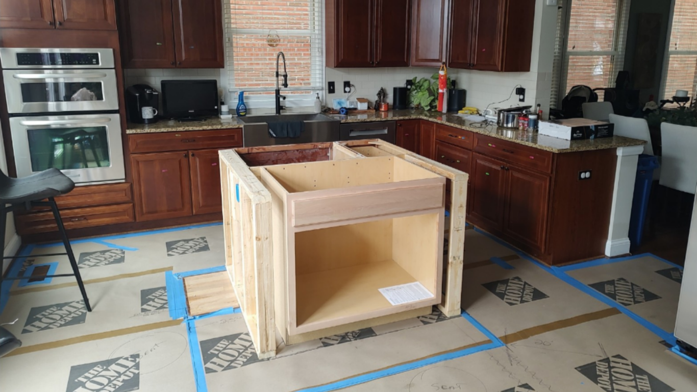 Kitchen with wooden cabinets, a built-in oven, and a black sink. There is a construction project in progress with a wooden frame. Blue painter's tape outlines the floor, which has Home Depot sheets covering it.