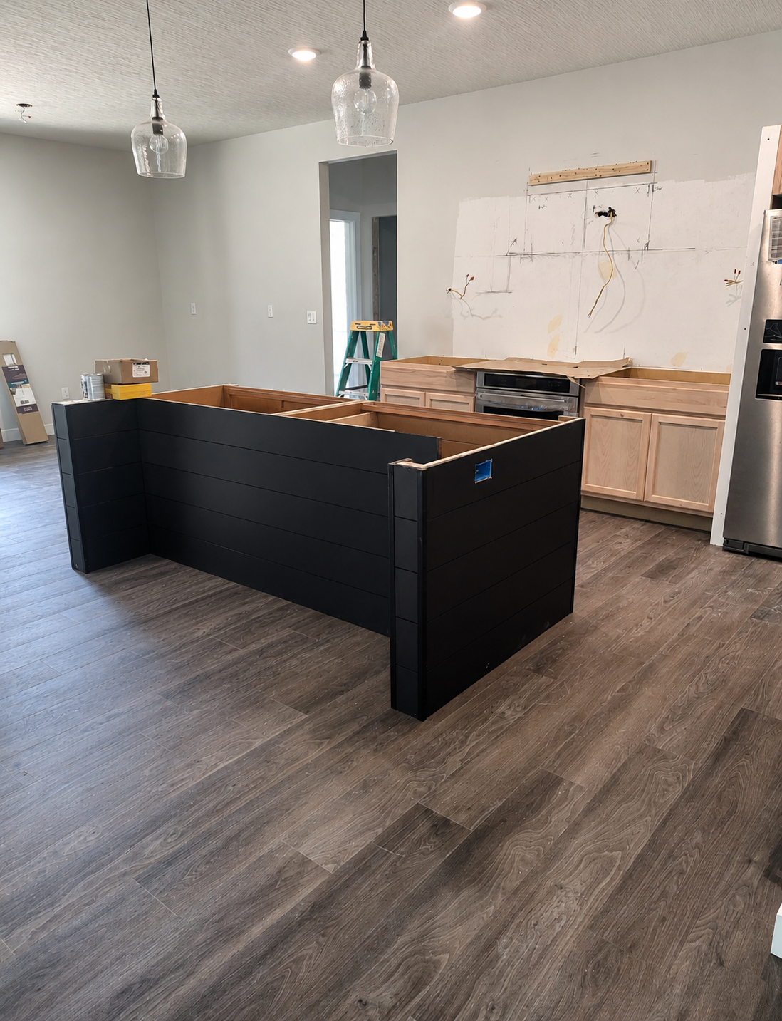 Kitchen remodel in progress featuring custom cabinetry installation, oversized black island, unfinished wood base cabinets, exposed electrical wiring, and luxury renovation details in Marengo, Ohio.