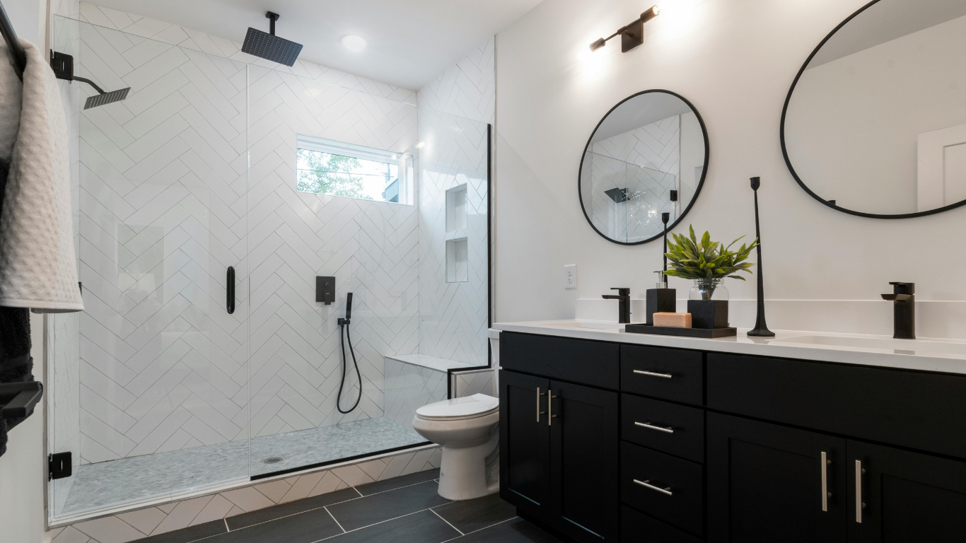 Modern bathroom with a black double vanity, round black-framed mirrors, matte black fixtures, and a glass-enclosed shower with white herringbone tile.
