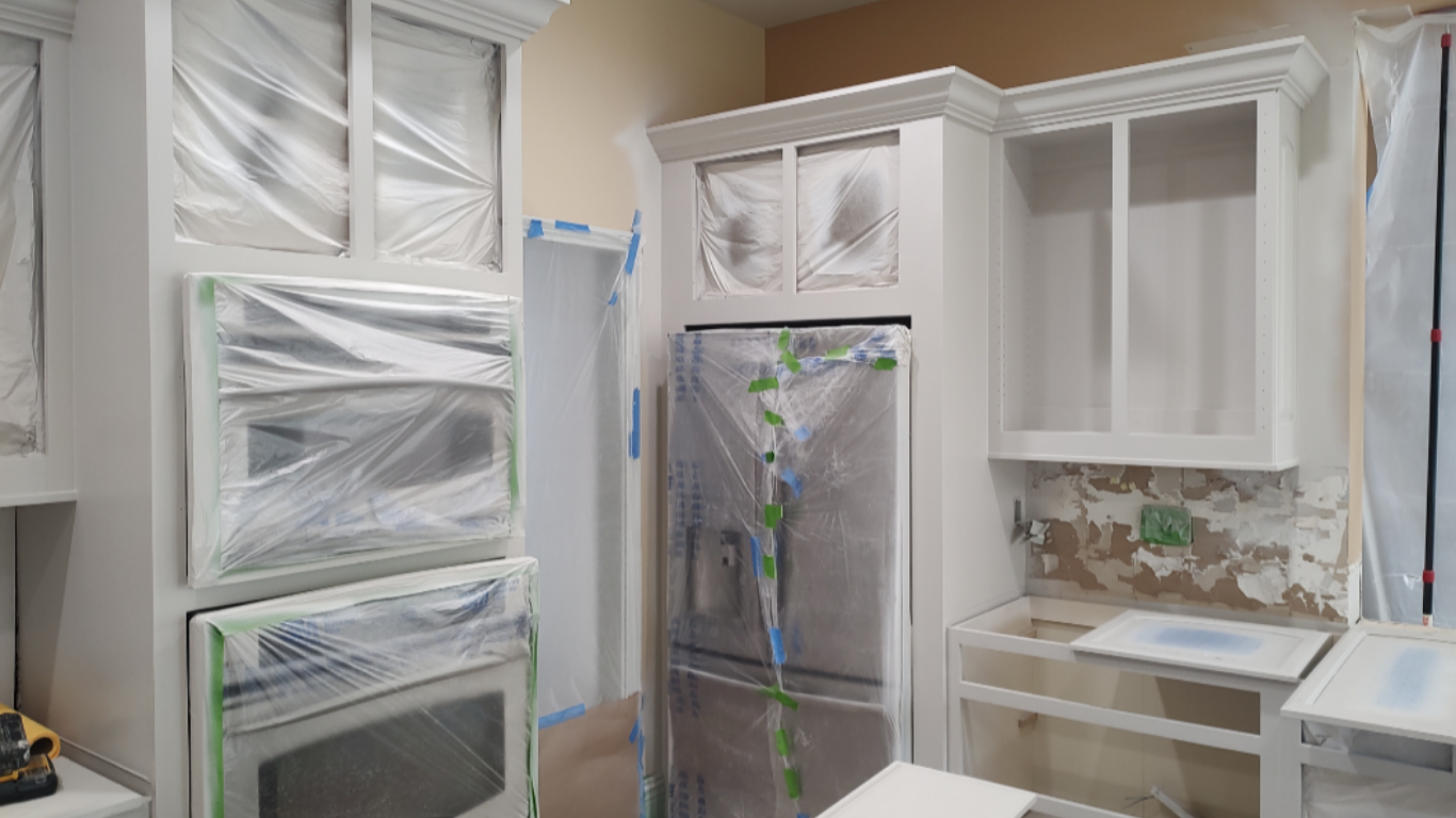 Freshly painted kitchen cabinet boxes with appliances masked in protective plastic film, prepared for new custom cabinet doors to complete the refacing project.