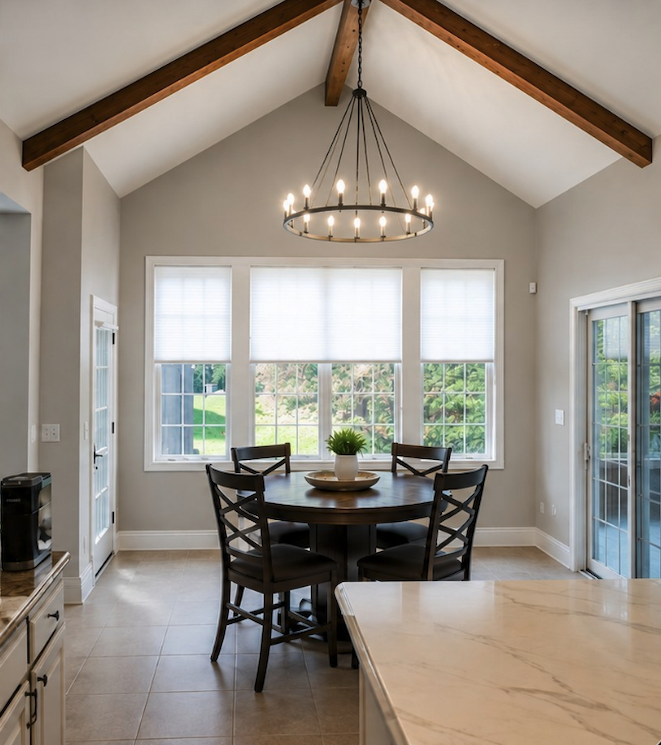 Dining area with a round table and five chairs, large windows with white blinds, a chandelier, and sliding glass door leading outside.