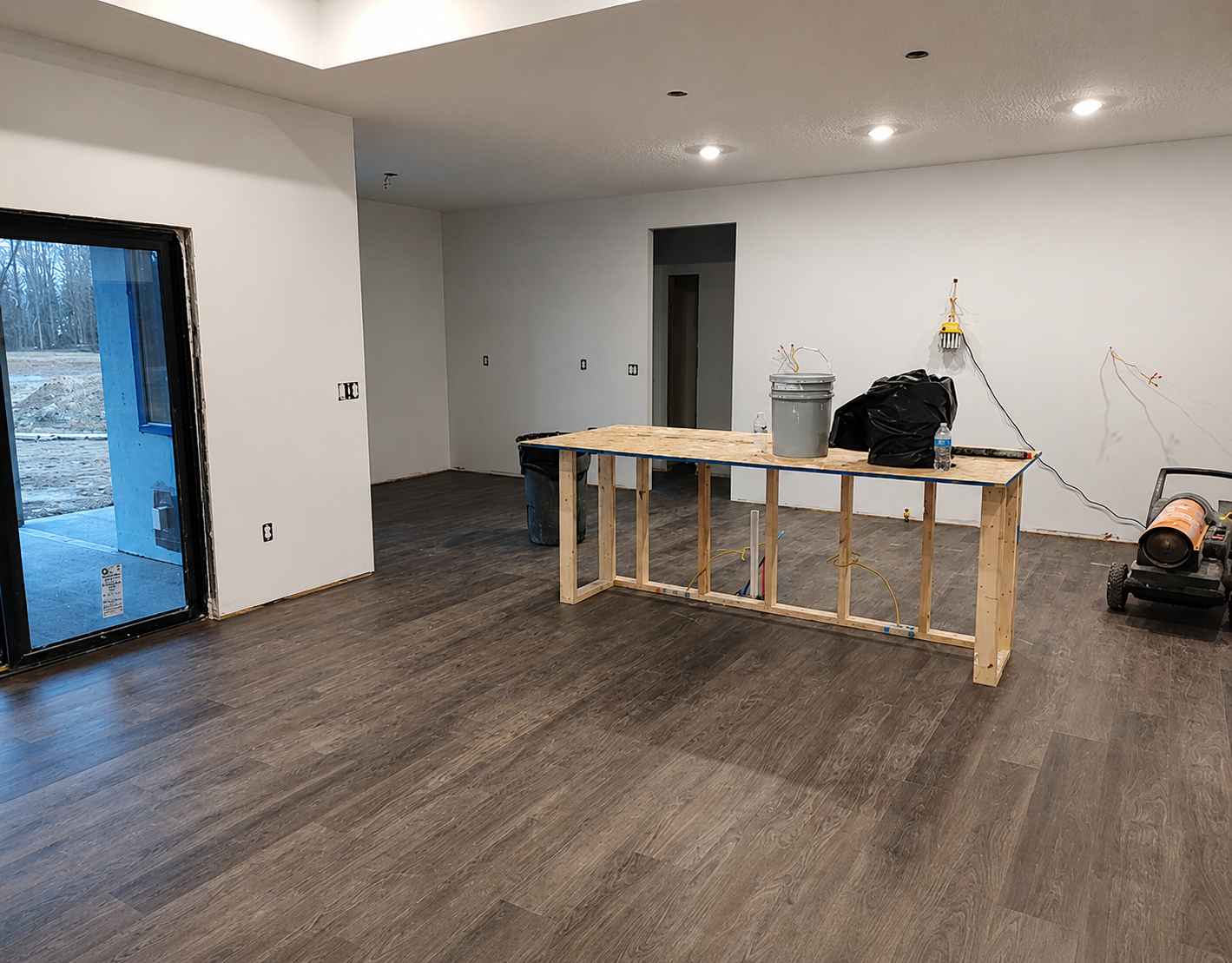 Luxury kitchen remodel before cabinet installation featuring newly installed flooring, recessed lighting, framed kitchen island, and open-concept layout during construction in Marengo, Ohio.