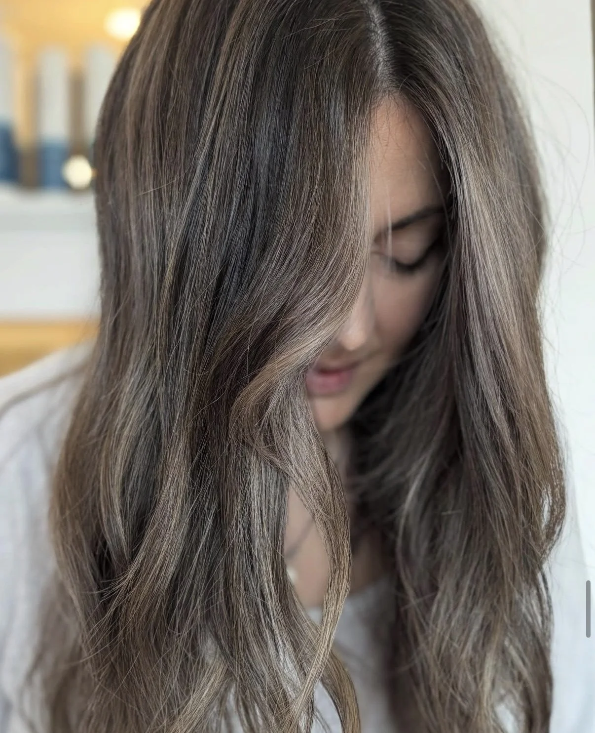 Close-up of a woman with long, wavy brown hair with highlights, looking downward.