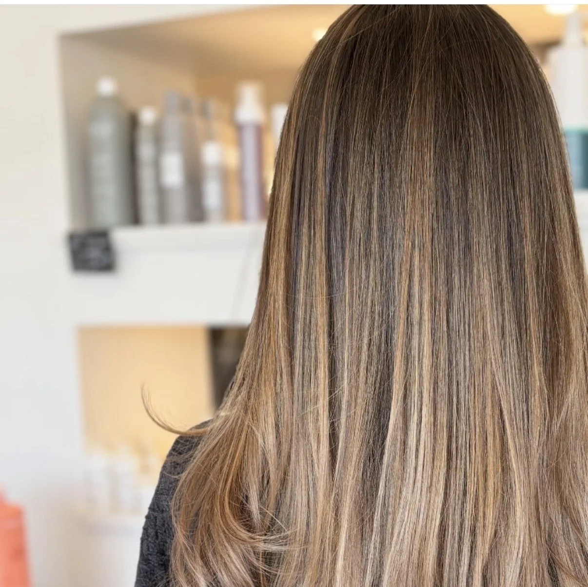 Back view of a woman with long, straight, ombre brown to blonde hair.