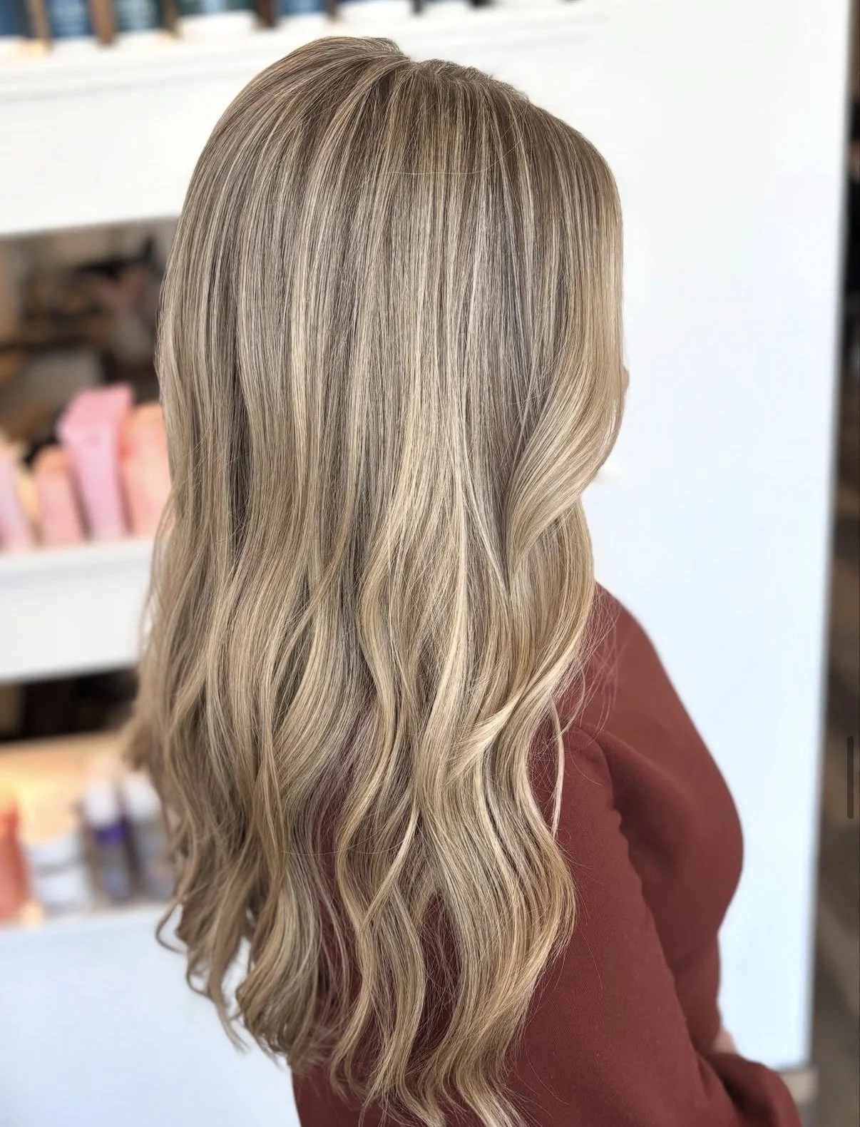Woman with long, wavy, blonde hair standing in front of shelves with hair products.