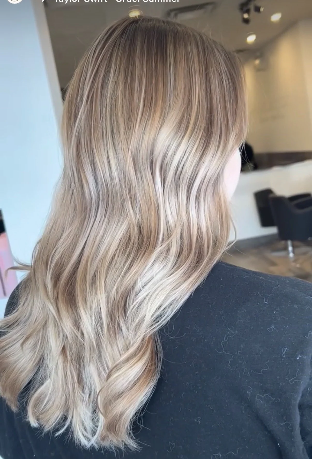 Back view of a woman's head showing long, wavy hair with blonde highlights in a salon setting.