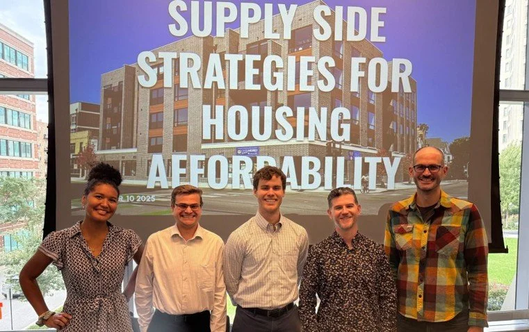 Group of five volunteers standing in front of presentation slide titled 'Supply Side Strategies for Housing Affordability' presented during a conference.