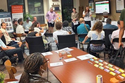 Volunteers sitting in a room, learning from presenters during the "Housing-a-Thon" educational event held in summer 2025.