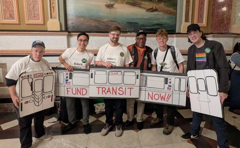 Six volunteers wore a train-themed "FUND TRANSIT NOW!!" costume in support of funding transit reform, 2025.