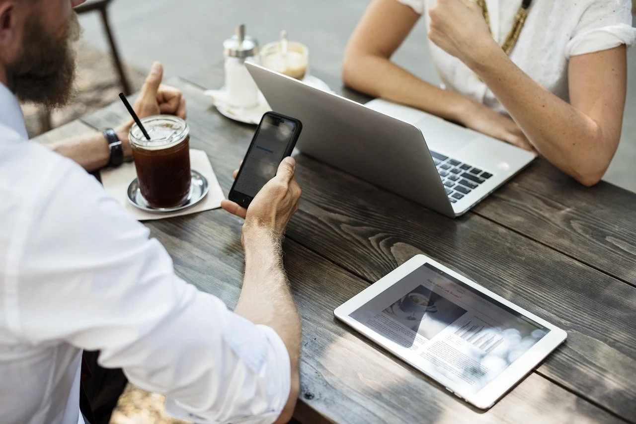 two people meeting over coffee, laptop, tablet and phone all on the table