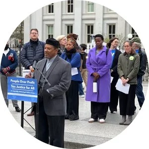 WE ORGANIZE - Photo of of Activists in DC speaking in front of sign that states "People over Profit"