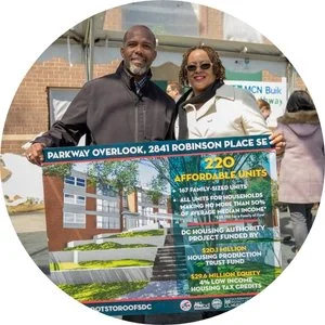 Photo of two people, a Black man and woman, holding a banner promoting Parkway Overlook, a block of 220 affordable housing units.