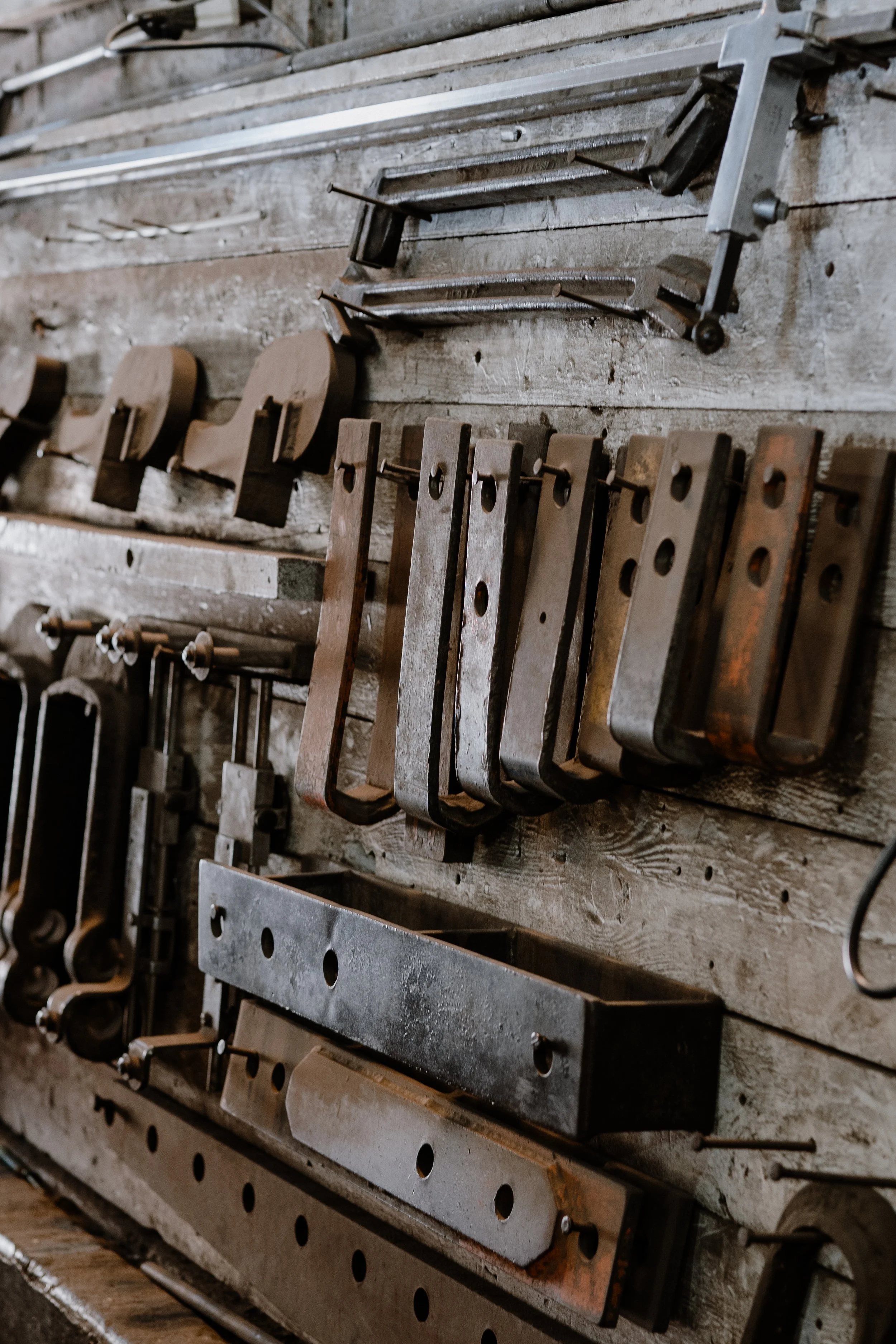 A wall mounted collection of various metal tools and clamps, some rusted, in a workshop or garage setting.